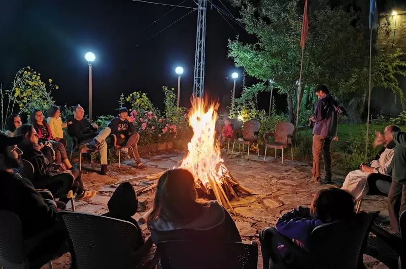 Students and mentors gathered around a campfire at night at E47 Base Camp