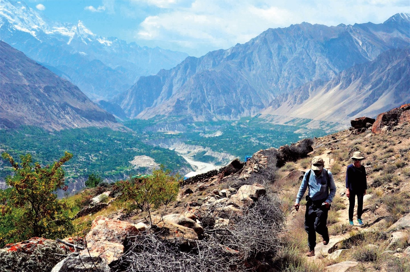 Two hikers on a mountain trail above the terraced fields and river of Hunza valley